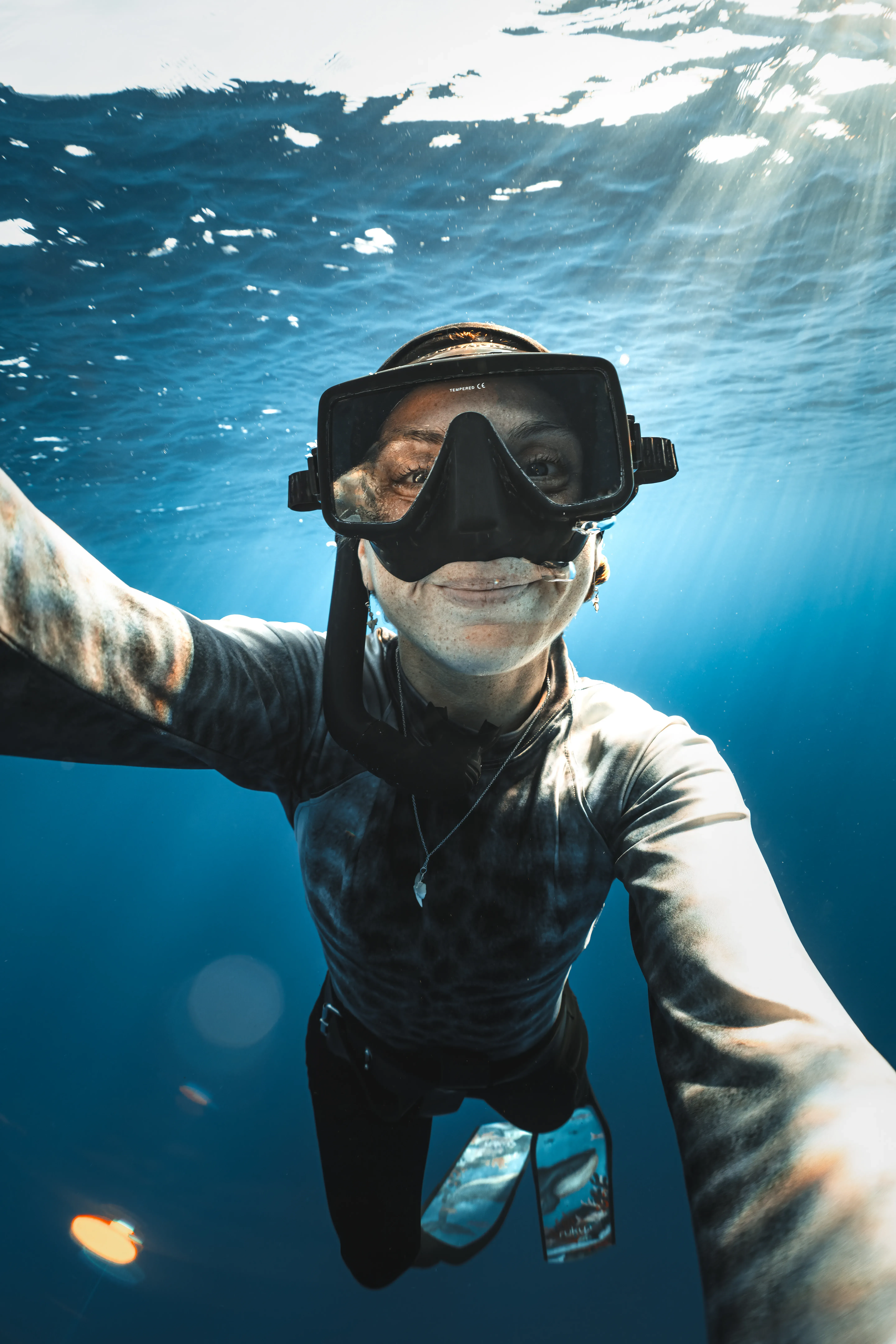 Sina Ritter smiling underwater in mask and snorkel, sunrays behind her — self-portrait in the blue